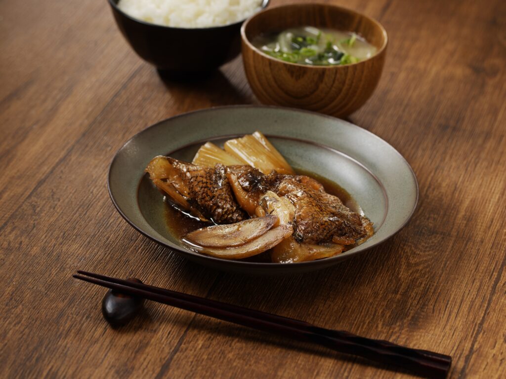 銀むつカマの煮付けが器に盛られ、ごはんと味噌汁とともに並べられた和風の食卓風景。煮汁が照り、ふっくらした身が美味しそうに映っている。