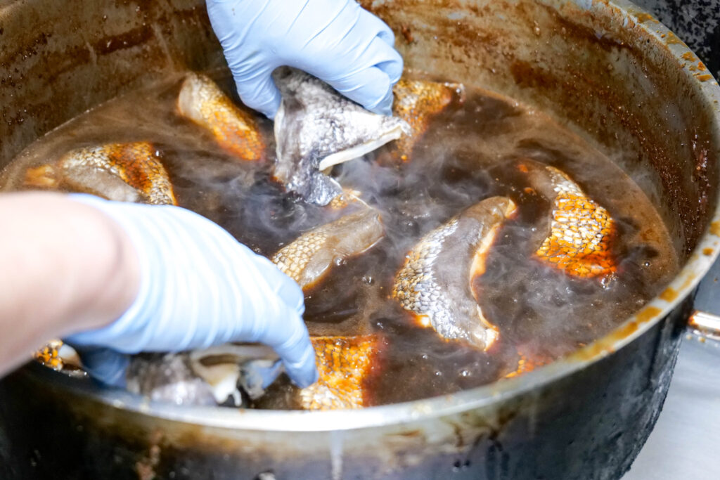 湯気の立つ九州らしい甘めのたれの鍋で、銀むつのカマを丁寧に煮付けている様子