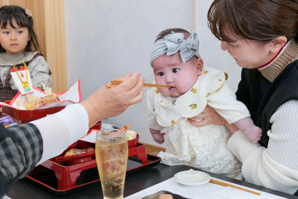 魚政のお食い初めで箸先を見つめる赤ちゃんのきょとん顔