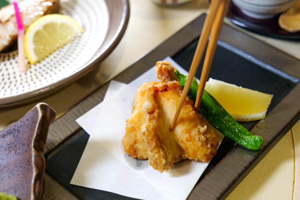 ふぐの唐揚げを箸で持ち上げた一口。衣の香ばしさが伝わるカット（魚政（うおまさ））