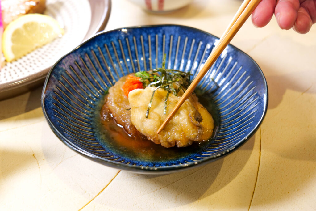 牡蠣の揚げ出しを箸で持ち上げた一口。香ばしさが伝わるカット（魚政（うおまさ））