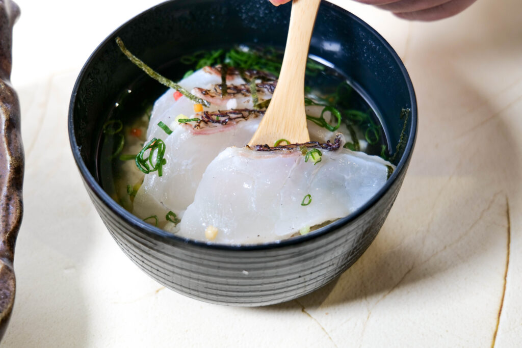 鯛だし茶漬けを箸で持ち上げた一口。出汁の温かさが伝わるカット（魚政（うおまさ））